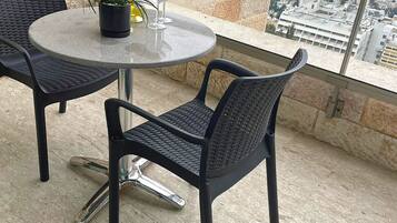 Una mesa redonda con dos sillas, una planta en maceta y una botella de aceite de oliva en un balcón con vista a la ciudad.