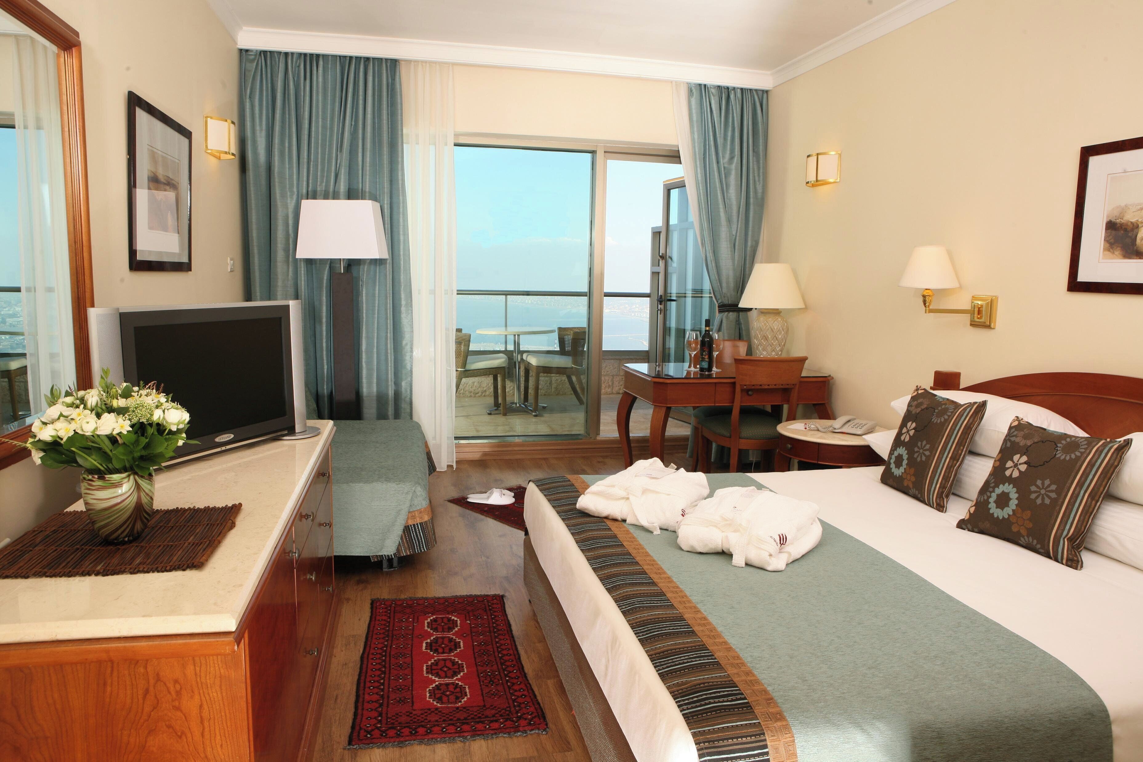 Ein Hotelzimmer mit Bett, Schreibtisch, Fernseher, Sessel, Tisch und Blick auf die Stadt.