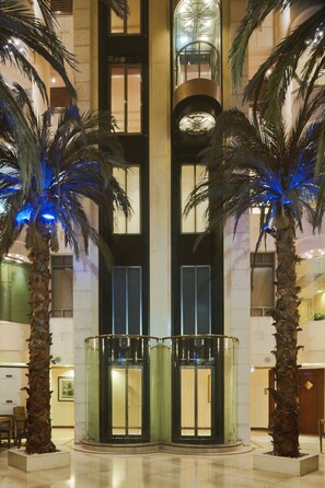 A lobby with two palm trees, a glass elevator, and a marble floor. - Crowne Plaza Haifa by IHG (Haifa)