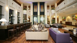 Um amplo hall de hotel com área de estar central, bar e uma grande janela.