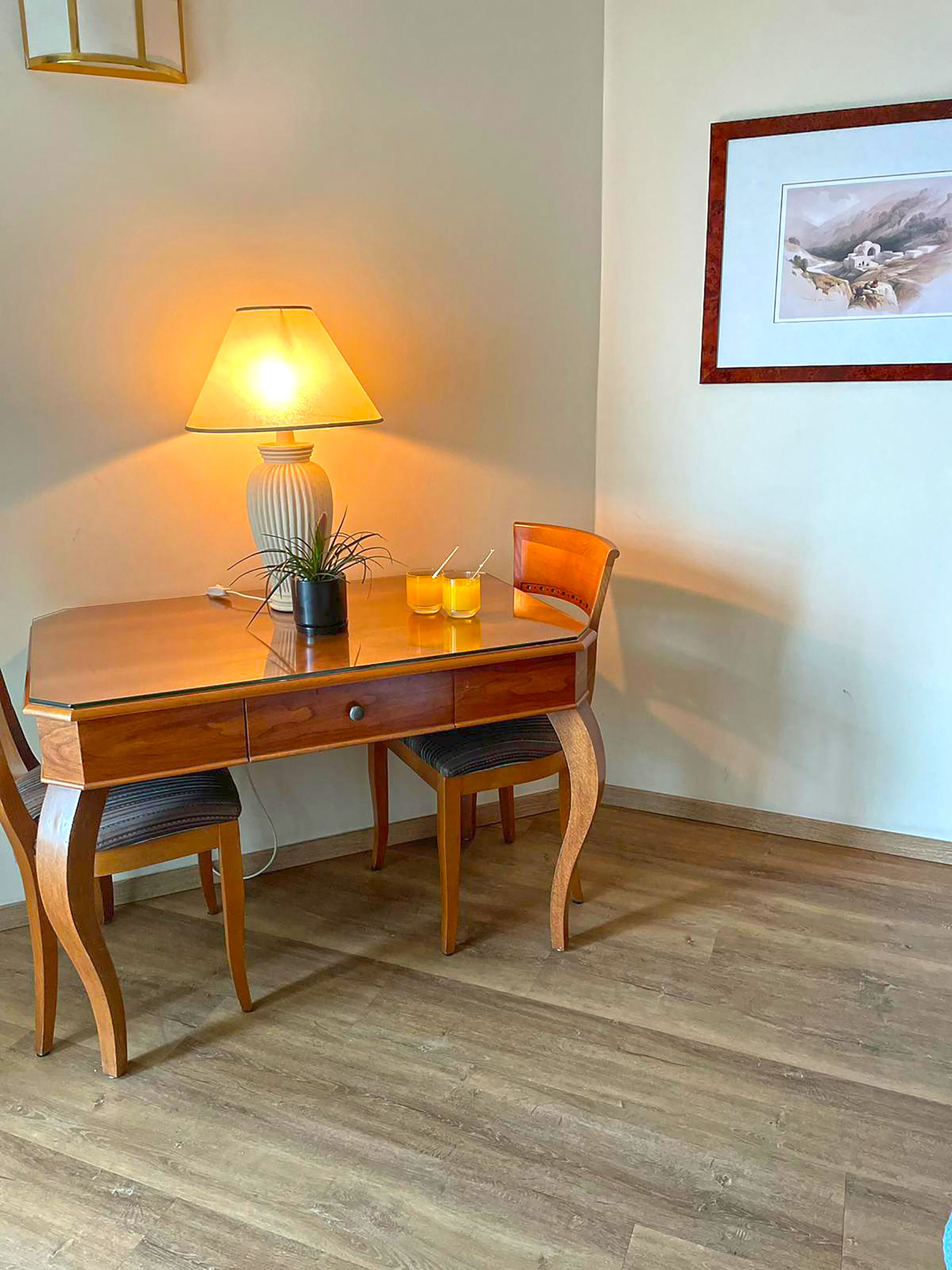 A wooden dining table with a lamp, two chairs, a small potted plant, and two glasses of orange juice.
