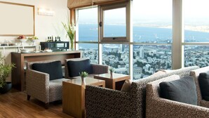 Uma sala de estar moderna com sofás estampados, uma mesa de centro e uma televisão. Uma grande janela oferece vista para a cidade.