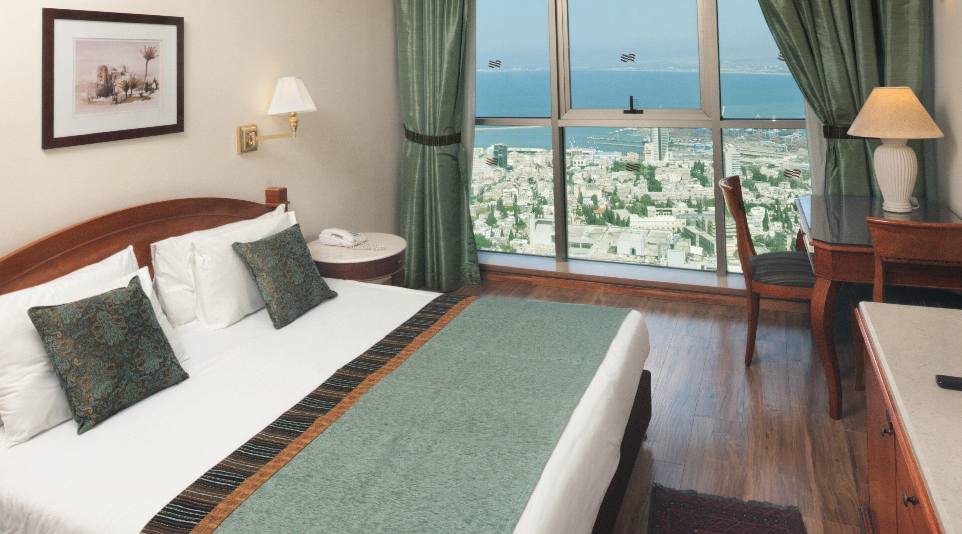 A hotel room with a large bed, a desk, a chair, a view of the city, and a window with curtains.