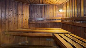 Una sauna con bancos y paredes de madera, un banco en primer plano y una lámpara en la pared.