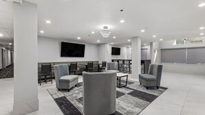 A modern hotel lobby with a seating area, a flat-screen TV, and a staircase.