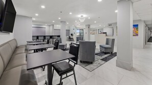 A modern hotel lobby with a seating area, a reception desk, and a large TV screen.