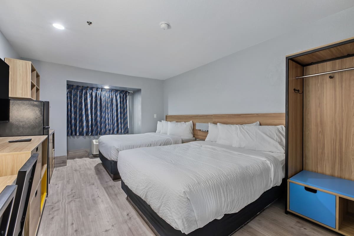 Une chambre d’hôtel avec deux lits, une armoire, un bureau et une fenêtre avec des rideaux.