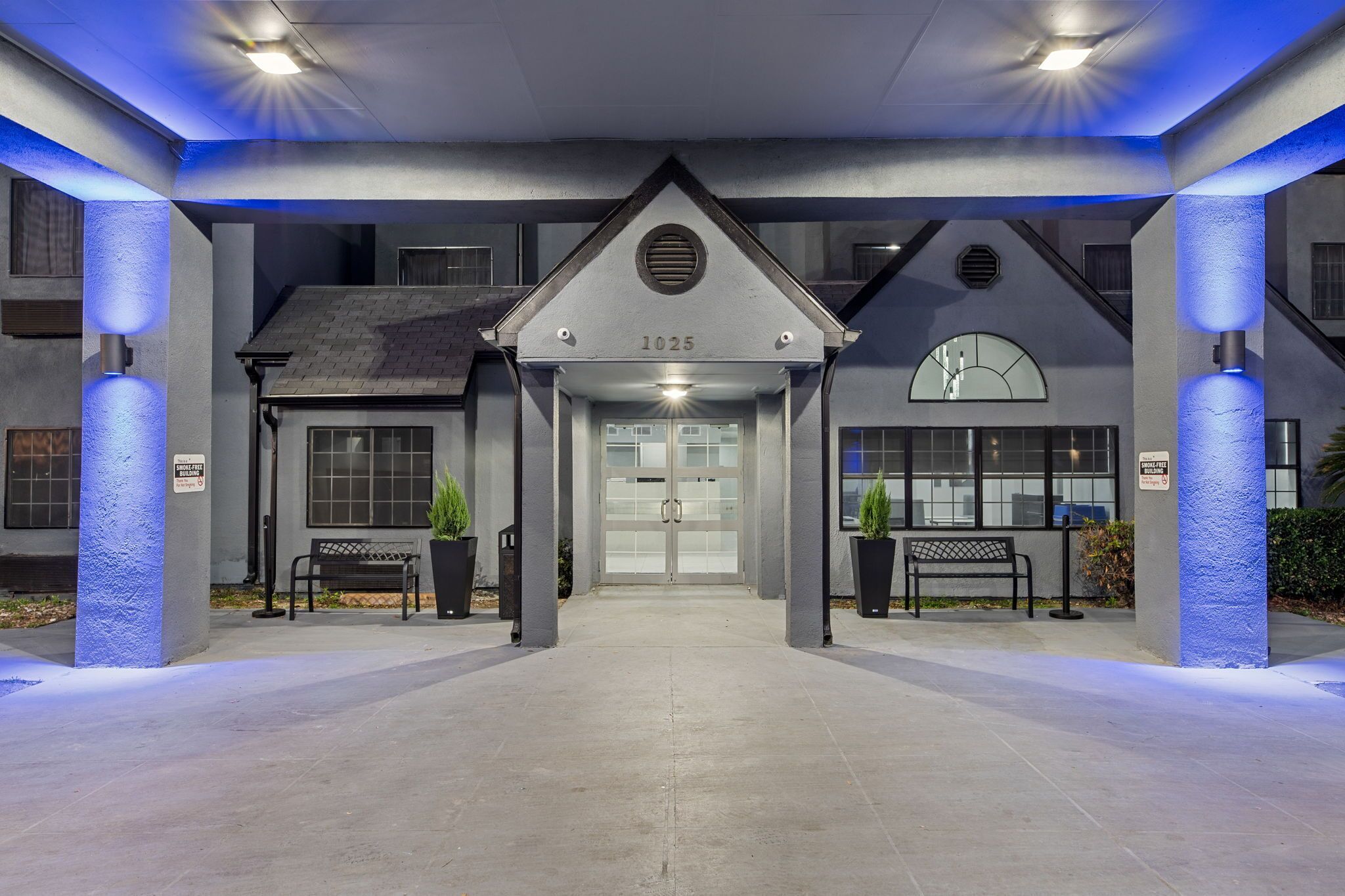 A hotel entrance with a modern design, featuring a numbered address sign, a clock, and a bench.
