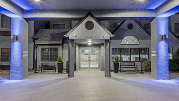 A hotel entrance with a modern design, featuring a numbered address sign, a clock, and a bench.