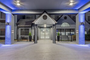 A hotel entrance with a modern design, featuring a numbered address sign, a clock, and a bench. - Days Inn by Wyndham San Antonio Downtown (San Antonio)