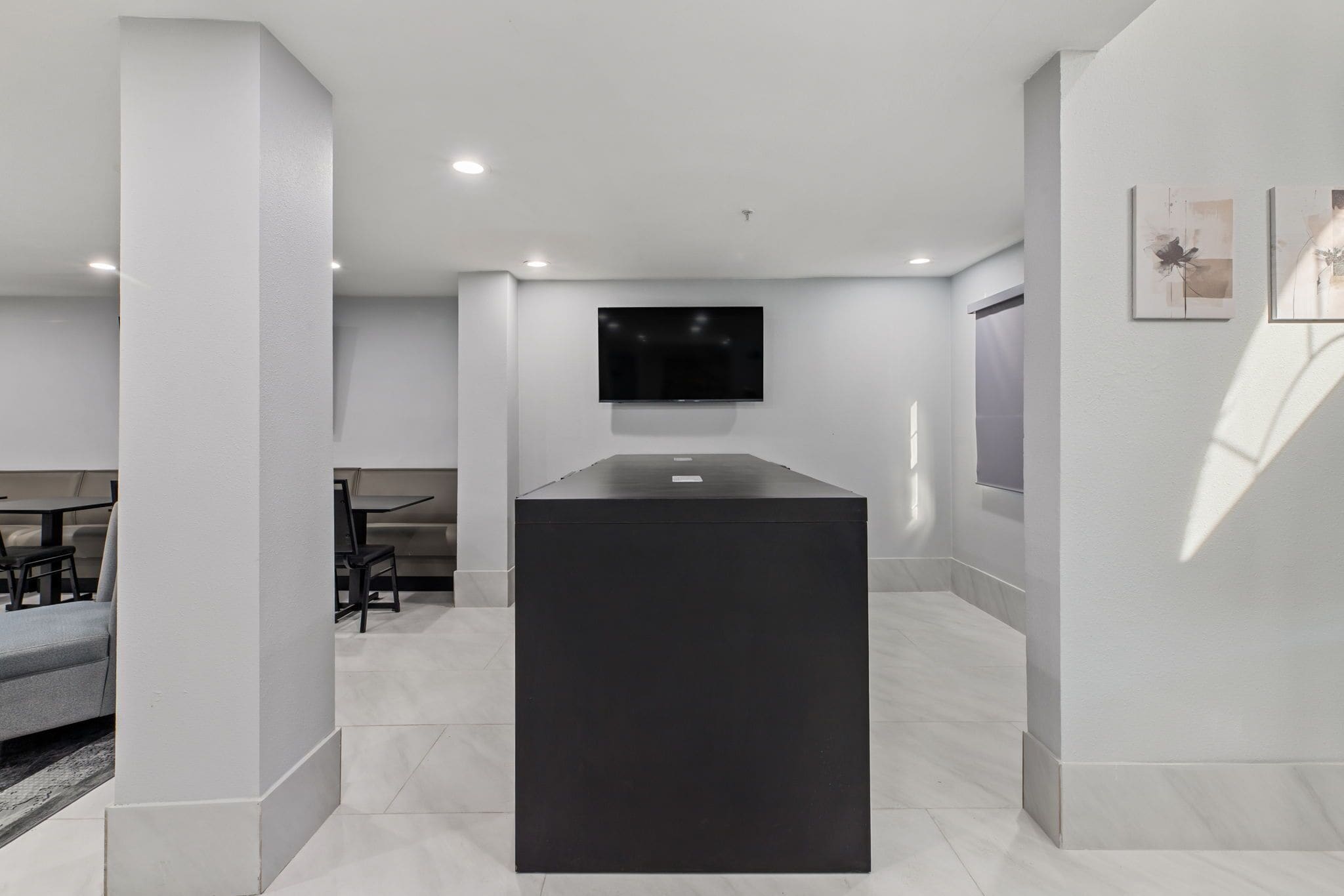 Una habitación de hotel moderna con un televisor de pantalla plana montado en la pared, una consola central de color oscuro y una zona de estar con sofá y sillones.