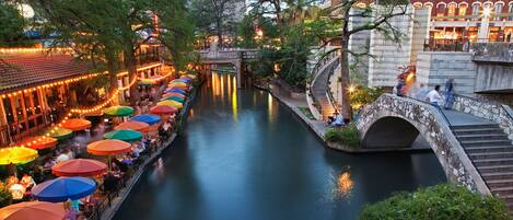 Un canal con un puente de piedra y un restaurante con sombrillas de colores a lo largo del agua.