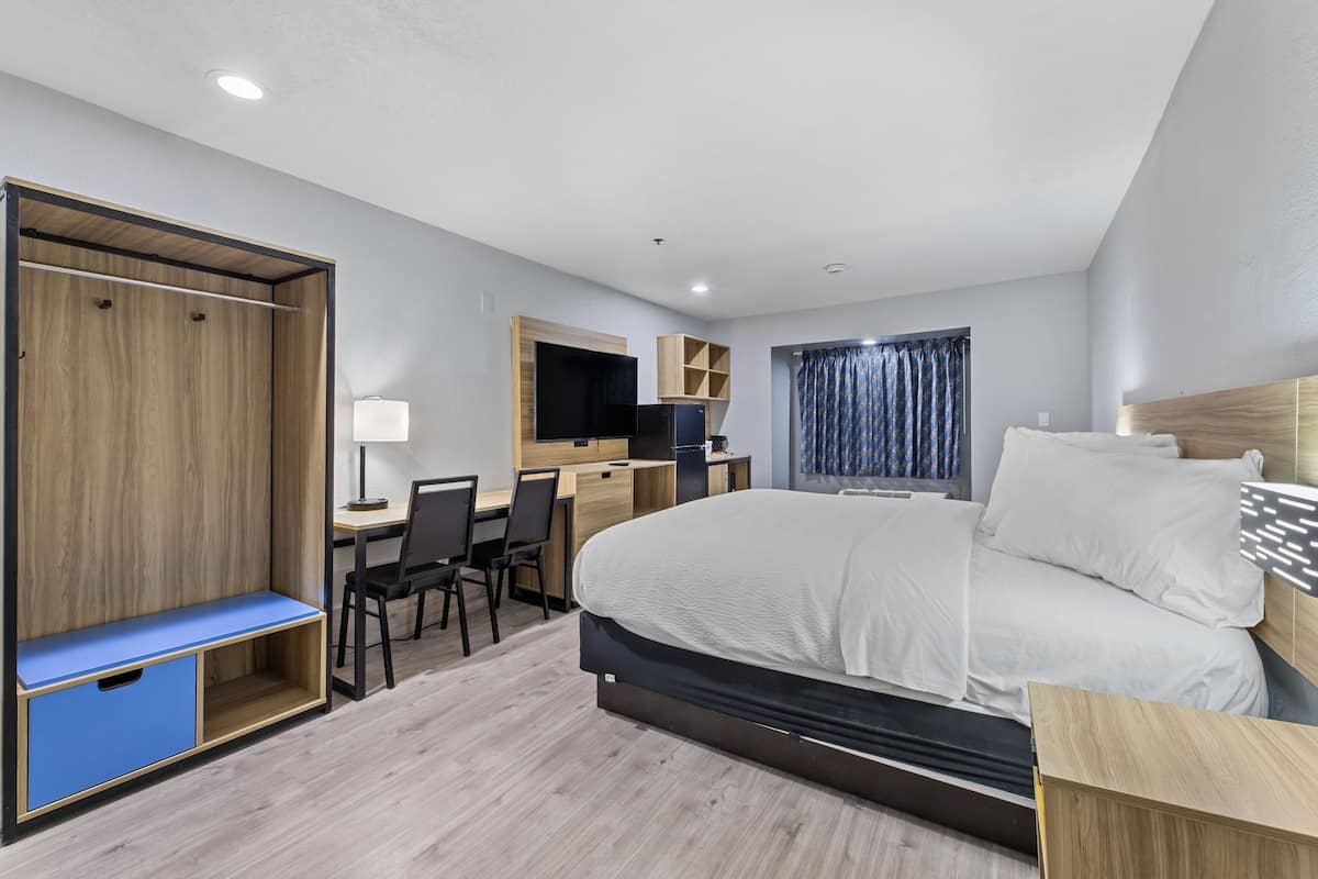Une chambre d’hôtel moderne équipée d’un lit, d’un bureau, d’une chaise, d’une armoire et d’une fenêtre avec des rideaux.