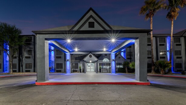 A hotel entrance with a covered area, palm trees, and a clear sky.