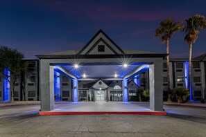 A hotel entrance with a covered area, palm trees, and a clear sky. - Days Inn by Wyndham San Antonio Downtown (San Antonio)