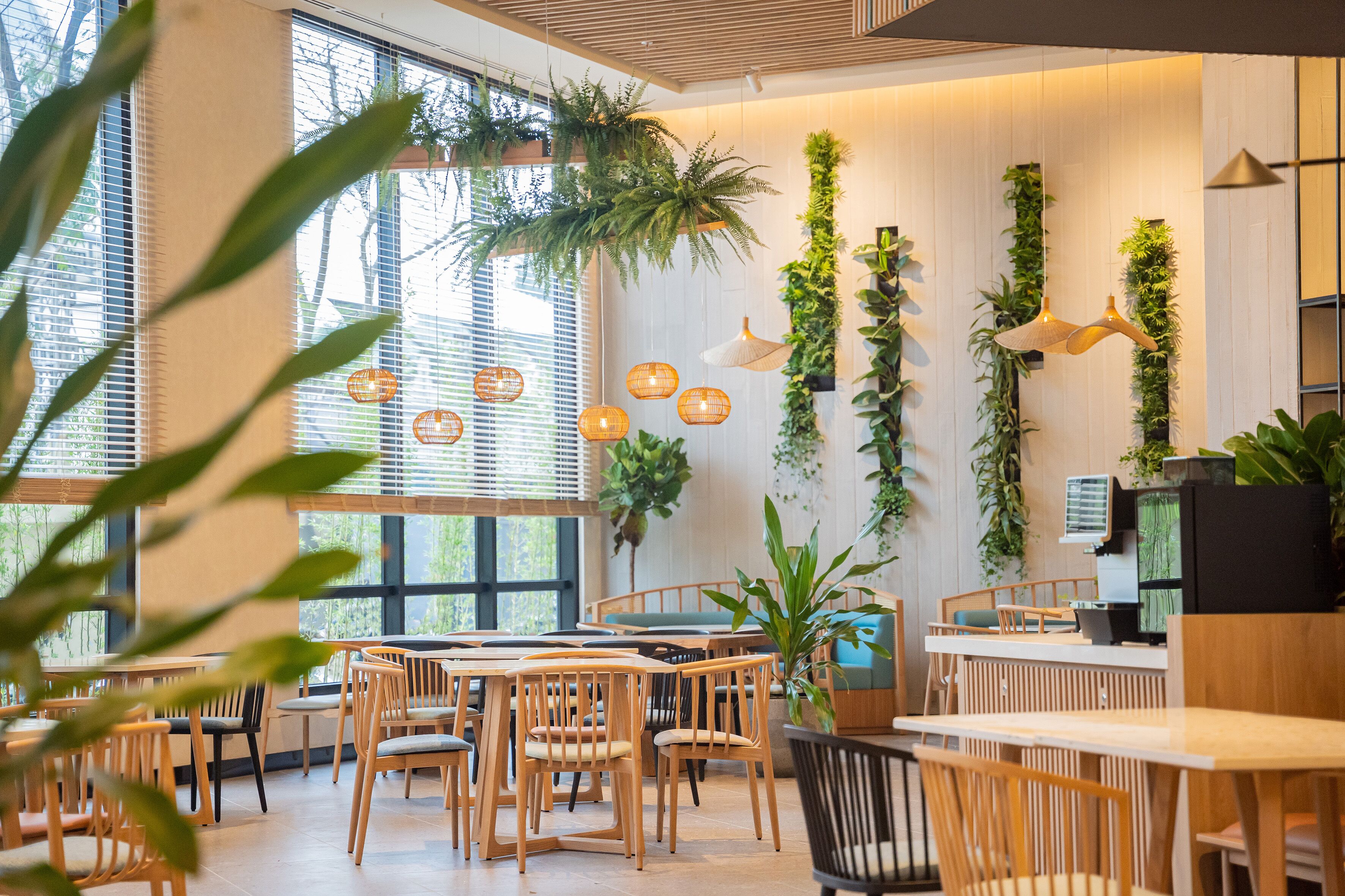 A modern cafe with wooden furniture, large windows, and vertical greenery.