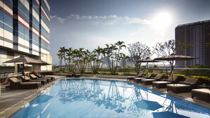 A rooftop pool with lounge chairs and umbrellas, surrounded by palm trees and modern buildings. - Melia Hanoi (Hanoi)