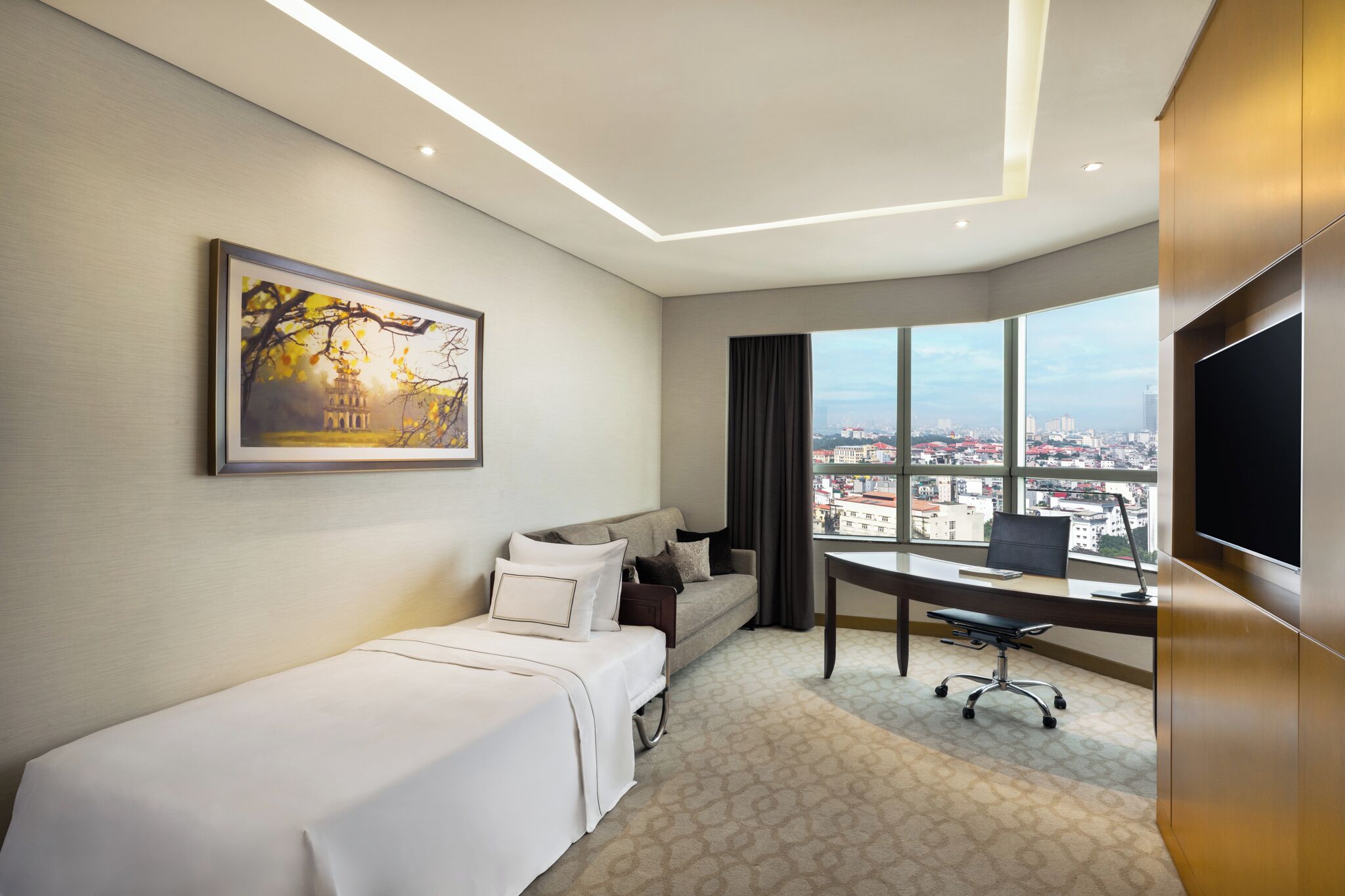 A hotel room with a bed, a sofa, a desk, a chair, a TV, and a large window with a city view.