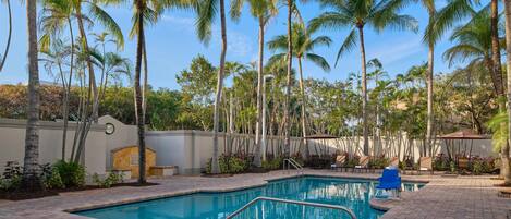 A swimming pool surrounded by palm trees and a patio area with seating.