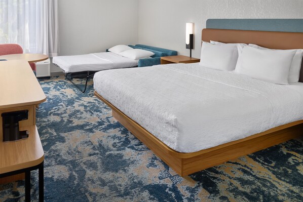 Una habitación de hotel con una cama, un escritorio, una silla, un sofá y una mesita de noche.