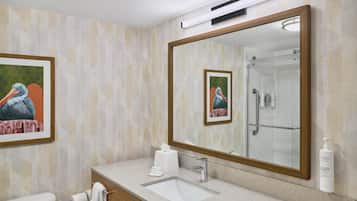 A bathroom with a large mirror, a sink, a toilet, and a shower.