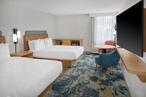 A hotel room with two beds, a desk, a chair, a television, and a view of the outdoors.