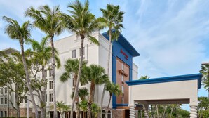 Un hôtel au design moderne, caractérisé par une palette de couleurs dominante en bleu et blanc, des palmiers et un ciel dégagé.