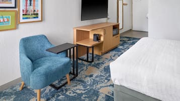 A hotel room with a bed, a desk with a coffee maker, a chair, and a TV on the wall.
