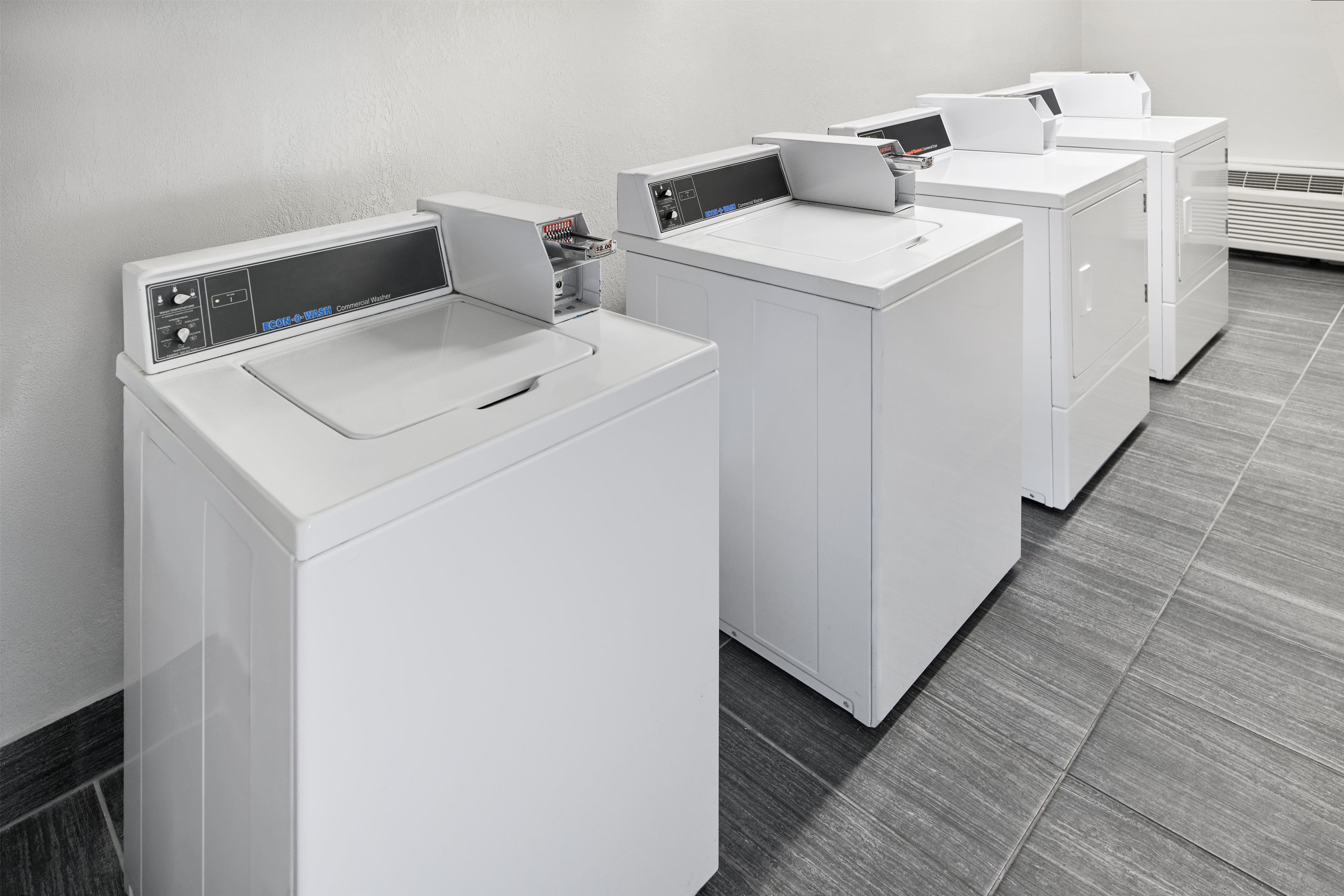 A row of white commercial washers in a room with a grey tiled floor.