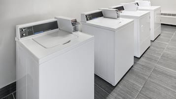 A row of white commercial washers in a room with a grey tiled floor.