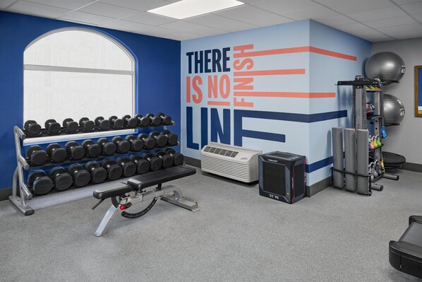 A gym with a wall mural, dumbbells, a bench press, and exercise balls.