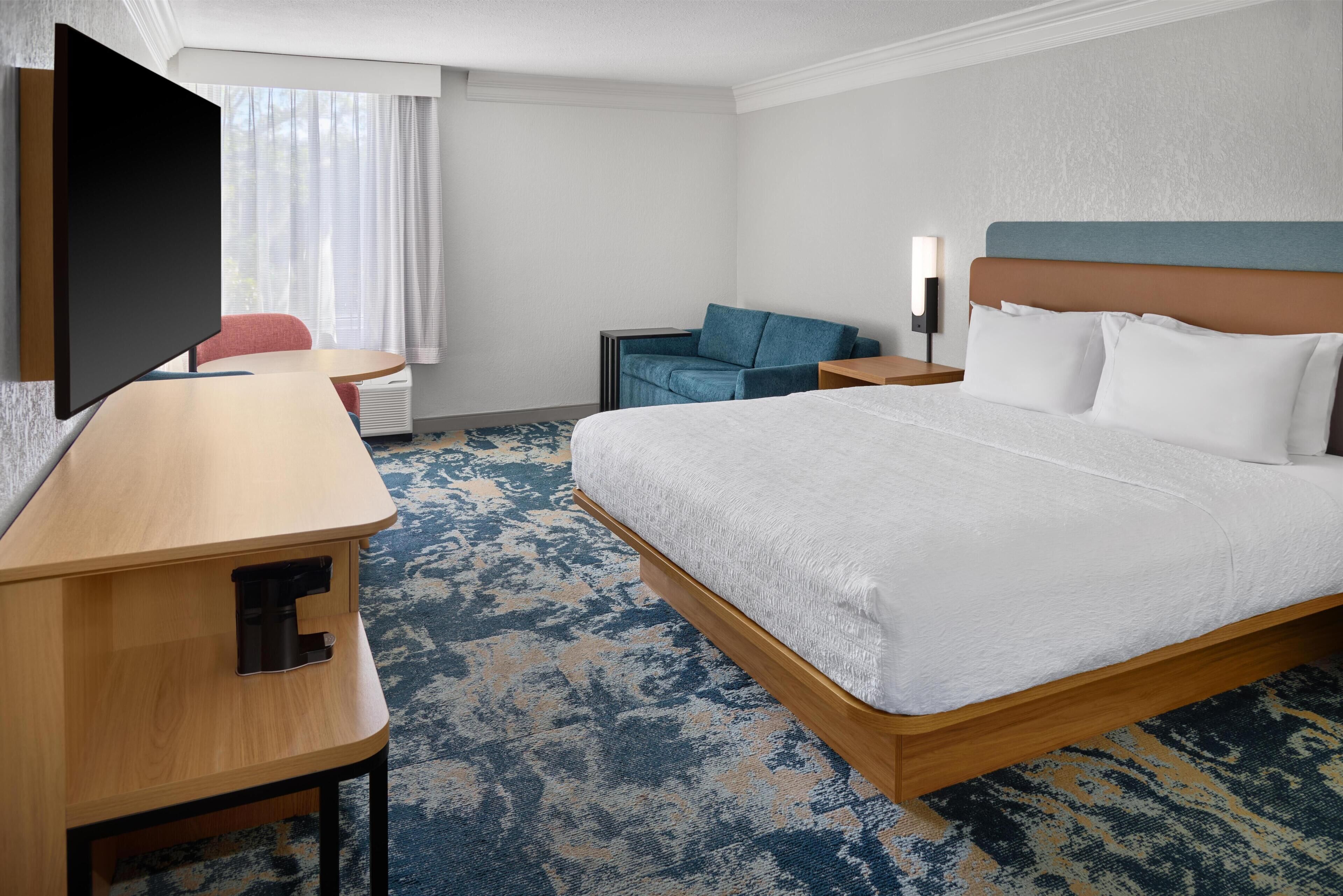 A hotel room with a bed, a desk, a chair, a TV, and a nightstand.