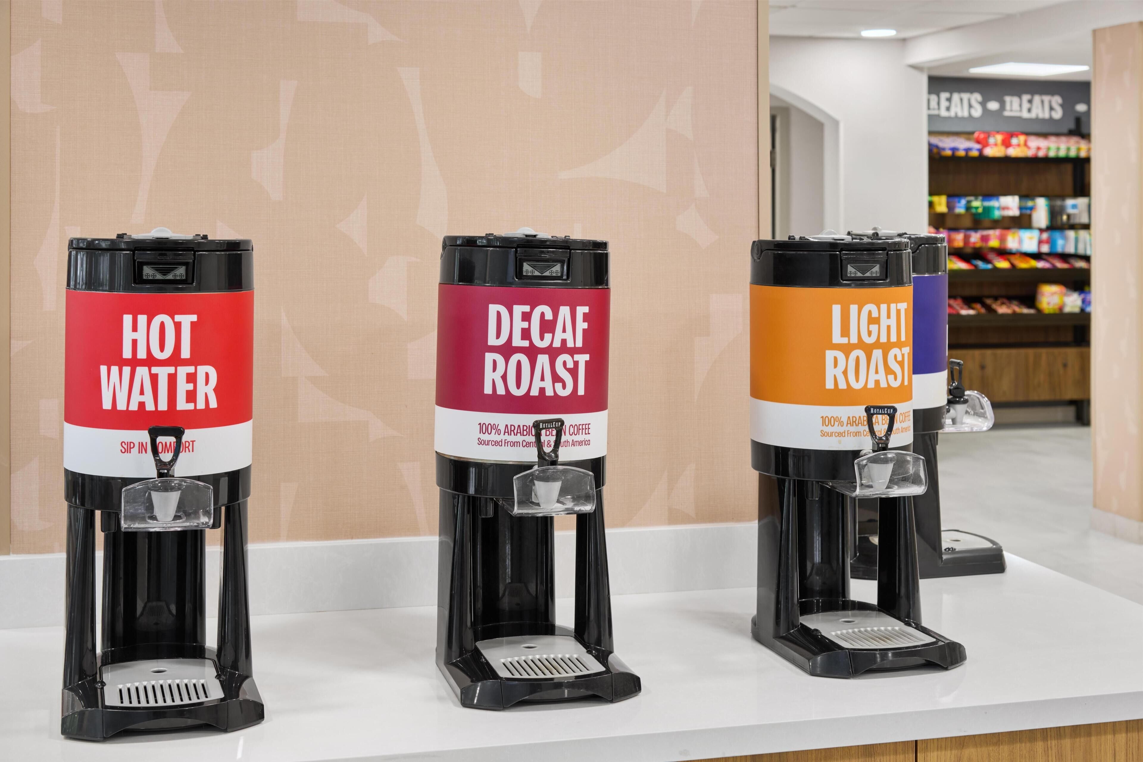 Three coffee machines labeled 'HOT WATER,' 'DECAF ROAST,' and 'LIGHT ROAST' on a counter.