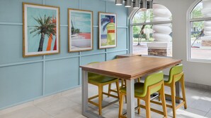 Un coin repas avec une table en bois et des chaises vertes, des œuvres d’art encadrées au mur et une vue à travers une grande fenêtre.