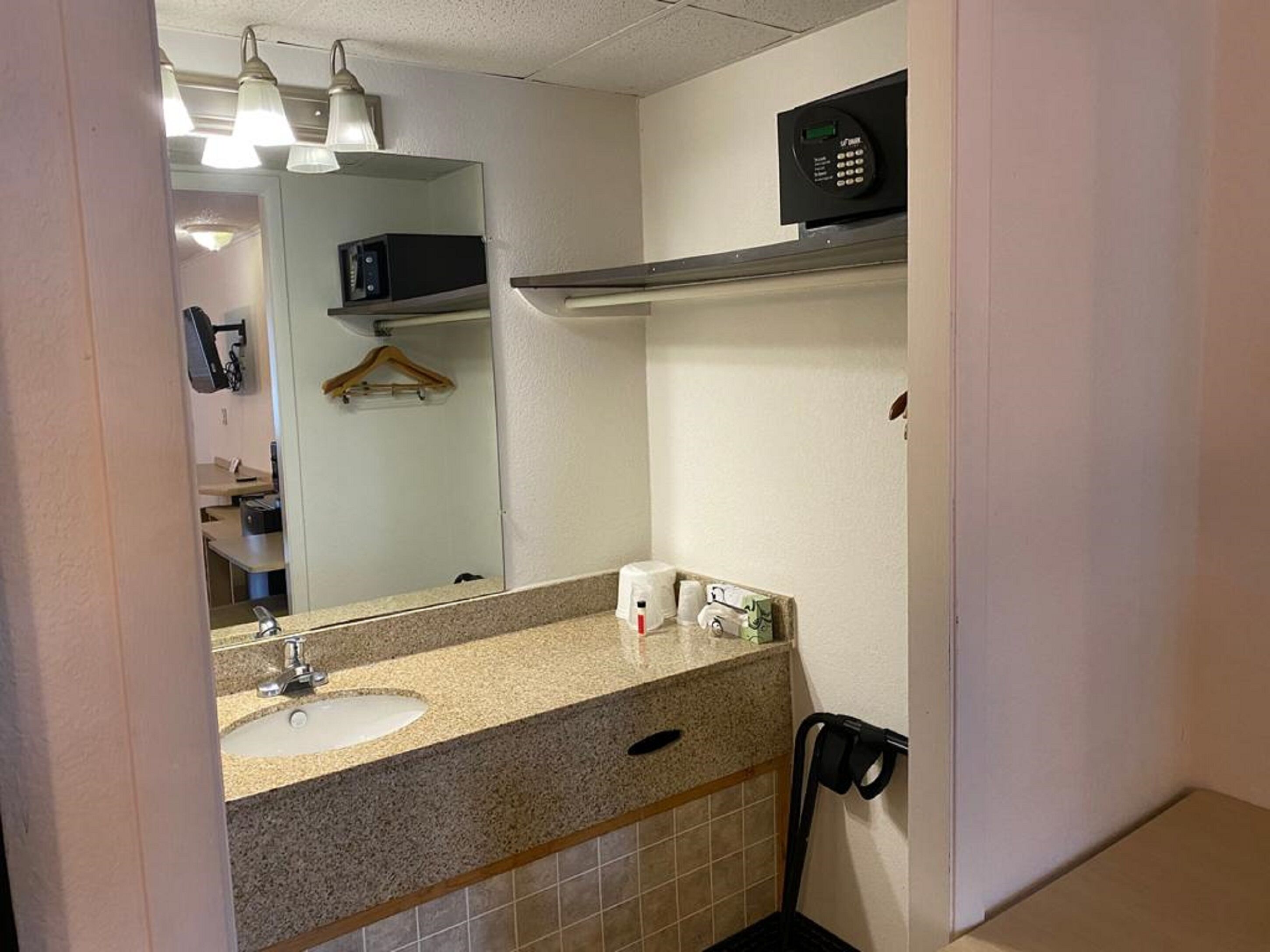 A bathroom with a sink, mirror, towel dispenser, and a microwave on the wall.