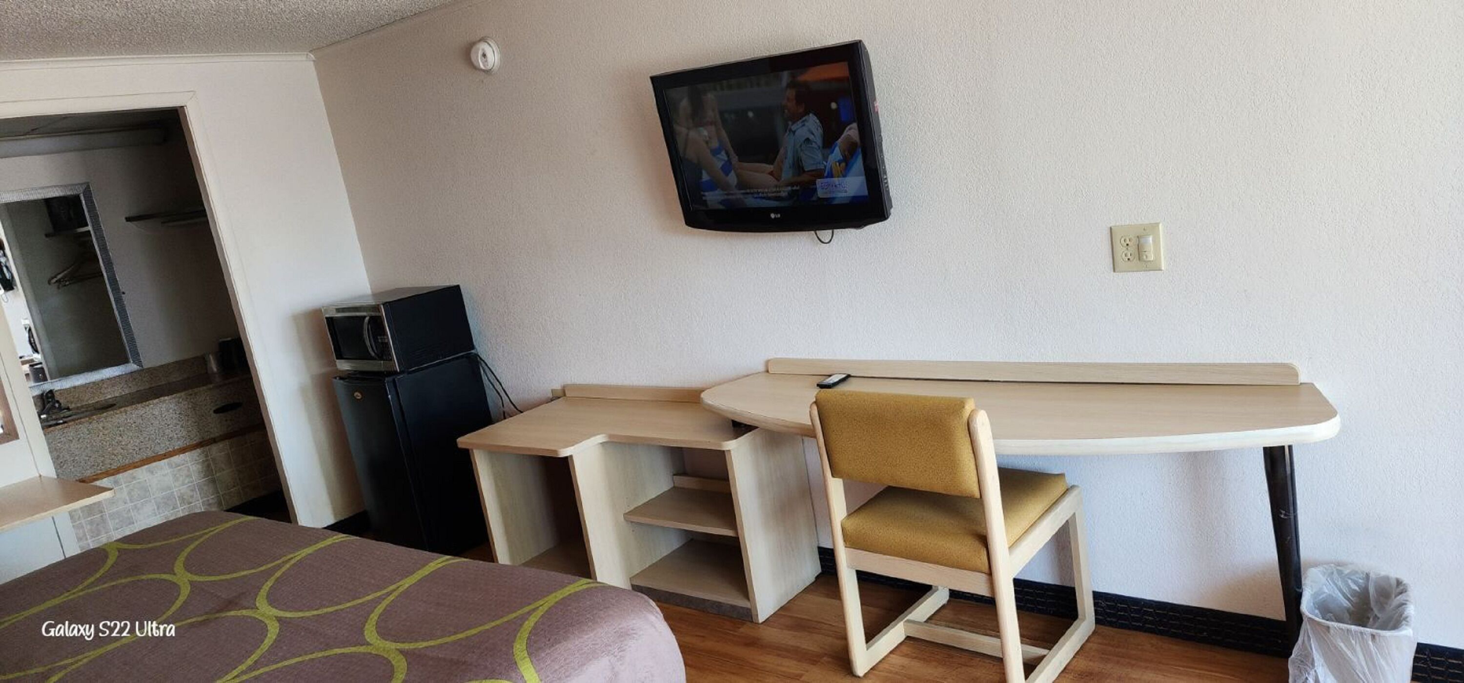 Una camera d'albergo con un letto, una scrivania con sedia, un televisore a muro e un angolo cottura.