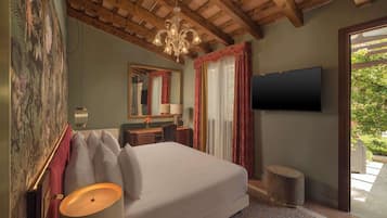 Un dormitorio con una cama grande, televisor, escritorio con lámpara y vista a zonas verdes.