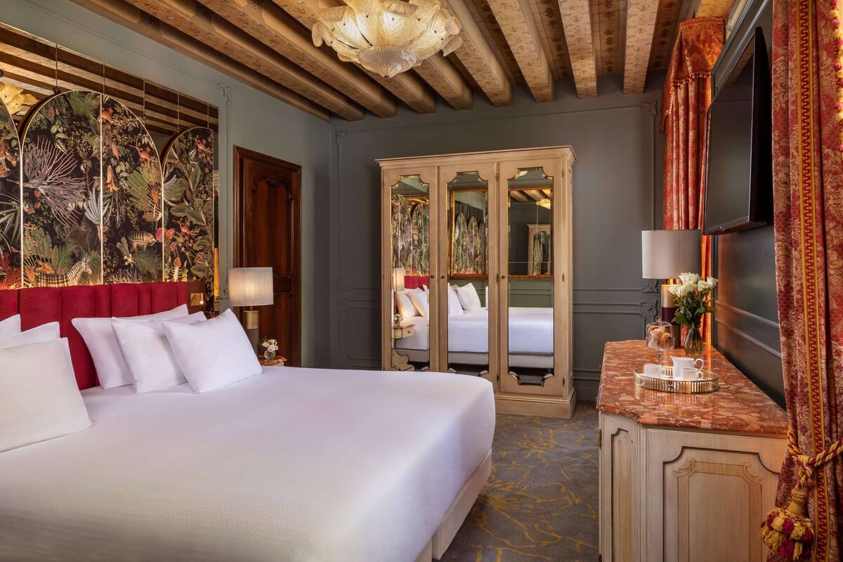 Een hotelkamer met een groot bed, een garderobe, een kaptafel met spiegel en een decoratieve plafondlamp.