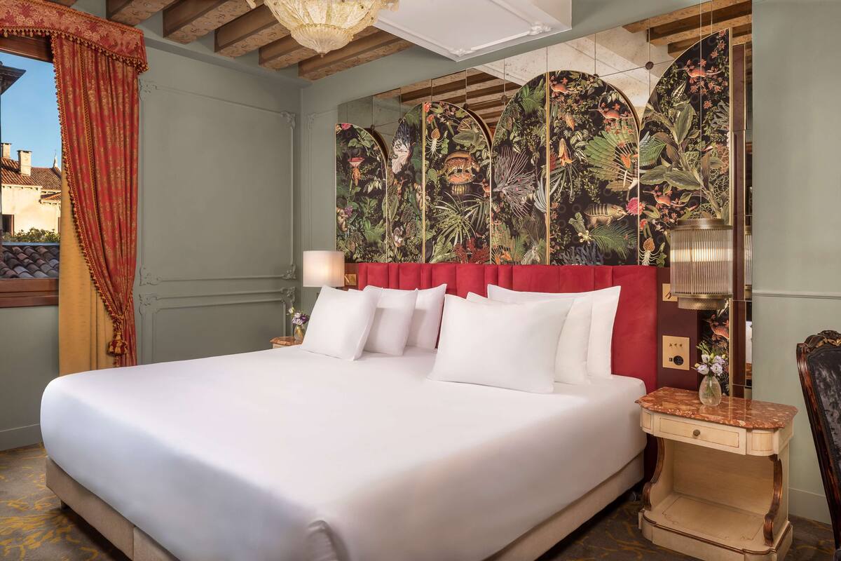 Een groot bed met witte lakens, een rode hoofdbord en een bloementapijt.