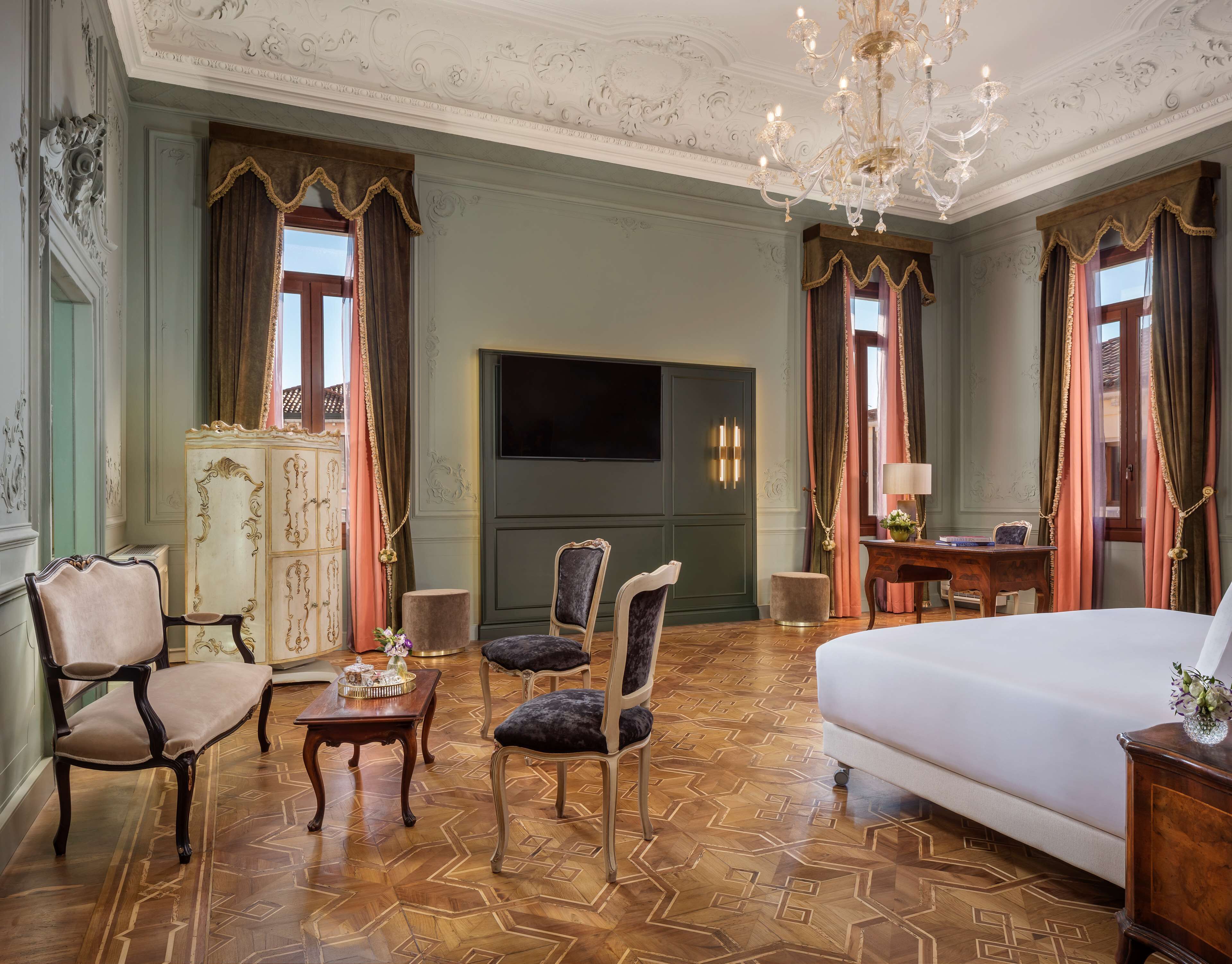 Een hotelkamer met een groot bed, twee fauteuils, een tafeltje, een bureau met lamp en een televisie aan de muur.