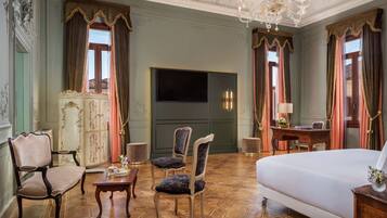 Een hotelkamer met een groot bed, twee fauteuils, een tafeltje, een bureau met lamp en een televisie aan de muur.