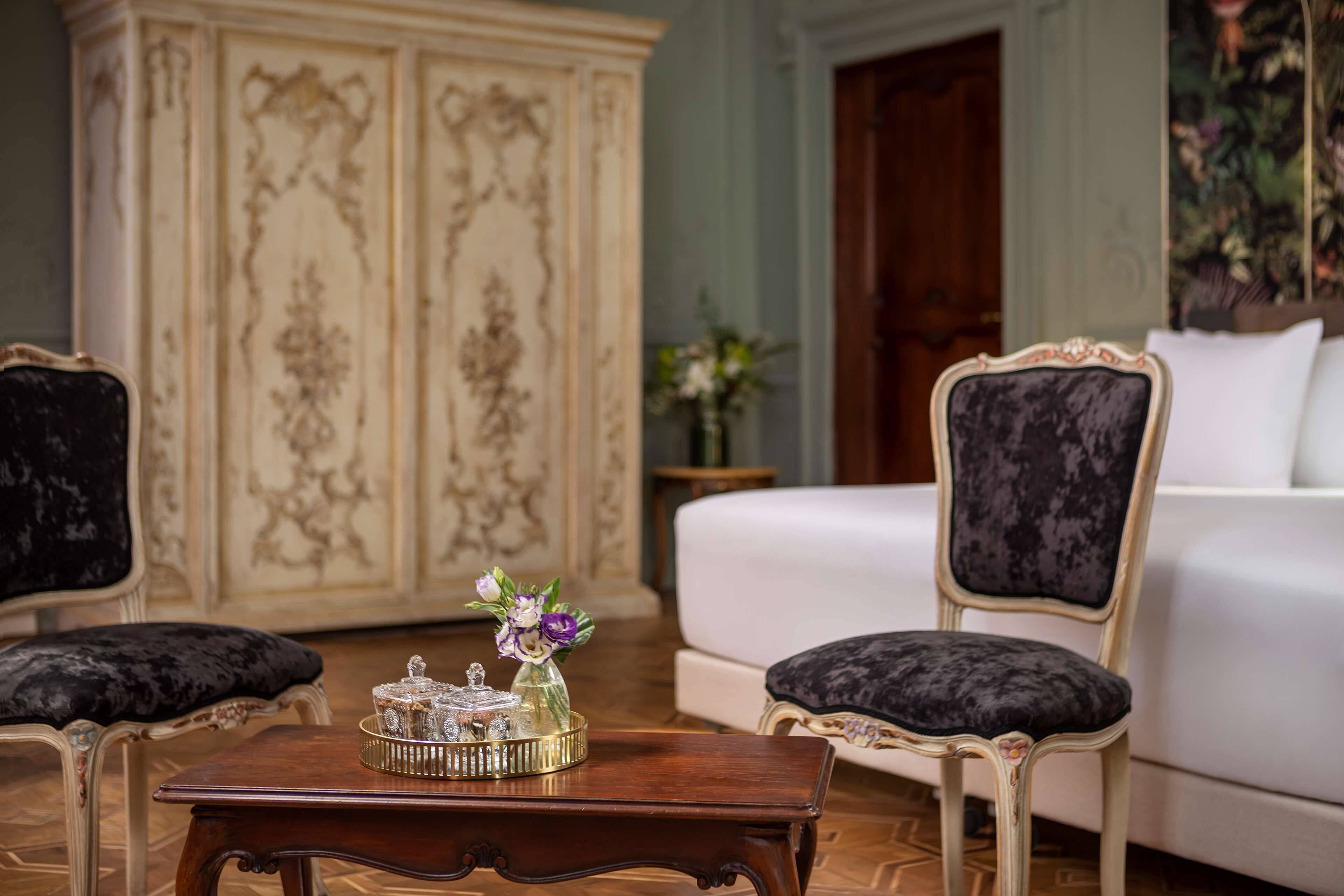 A room with a white sofa, two upholstered chairs, a wooden coffee table with a decorative item, and a large ornate cabinet.