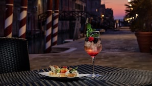 A table with a glass of cocktail garnished with mint and berries, and a plate of appetizers. - NH Collection Venezia Grand Hotel Dei Dogi (Venice)