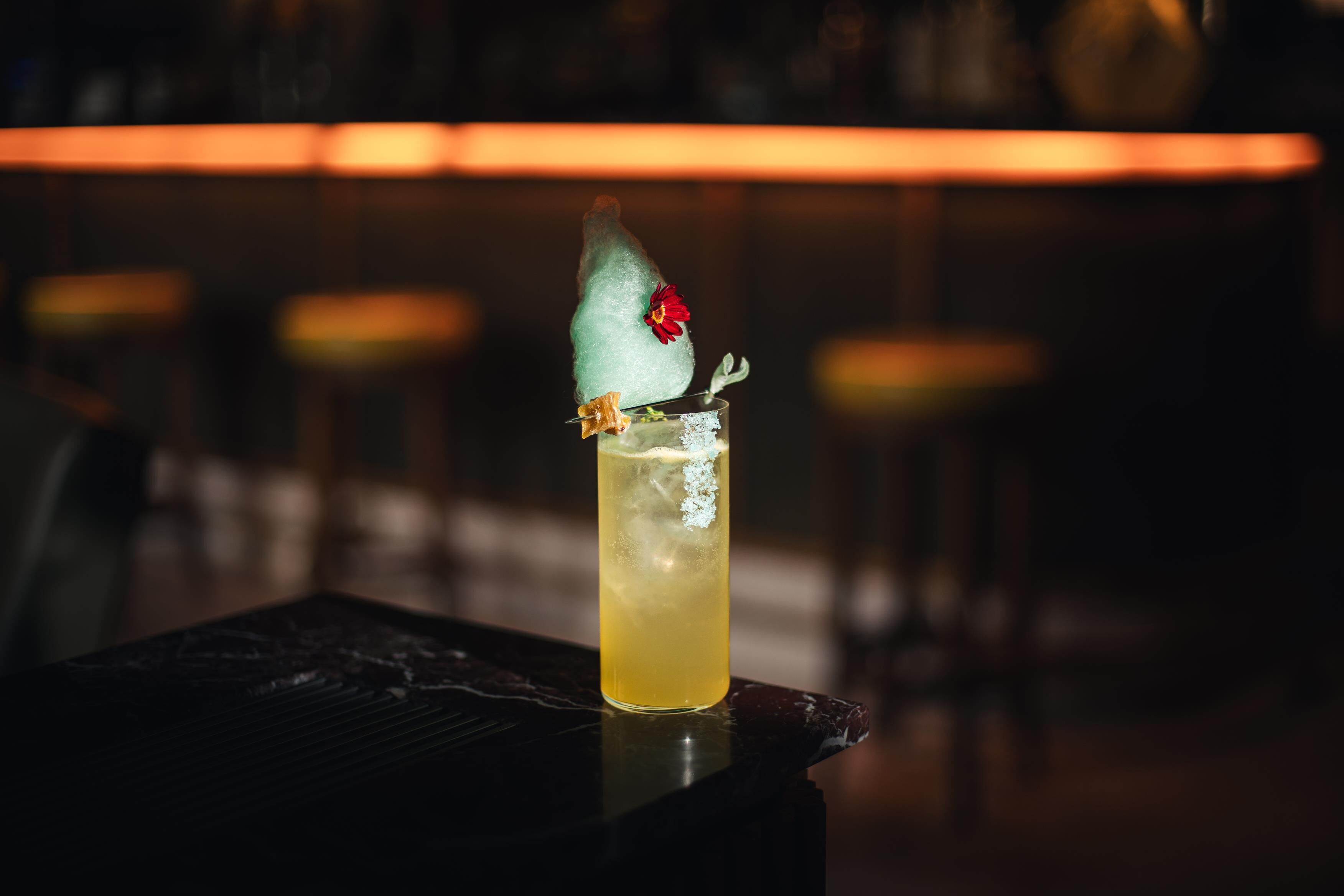 Ein Cocktail mit einer verzierten Eiskugel und einer Blume auf einer Bar.
