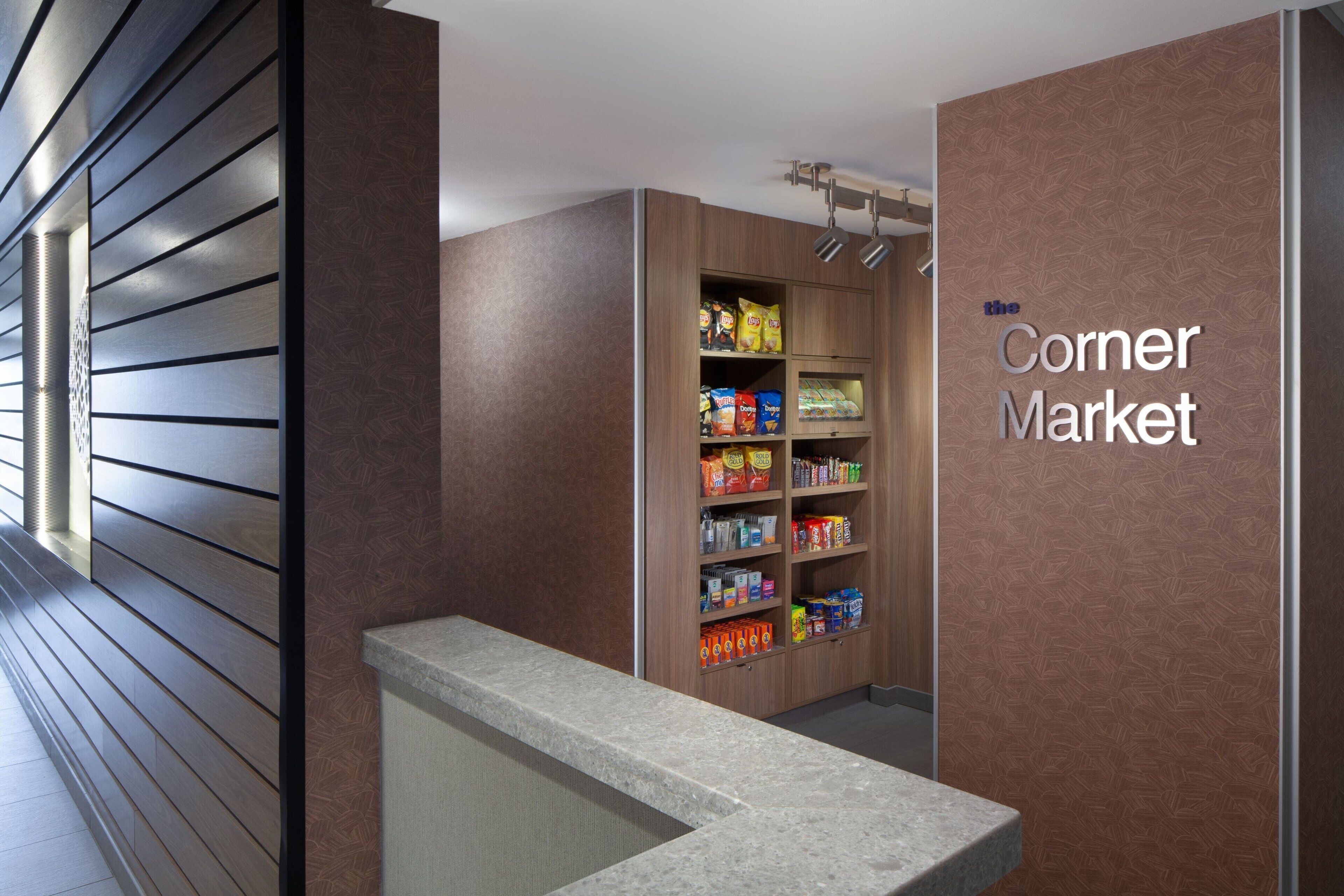 A corner market with a variety of packaged goods on shelves, a marble counter, and a patterned wall.