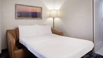 A hotel room with a bed, a chair, a lamp, a door, and a framed picture on the wall.