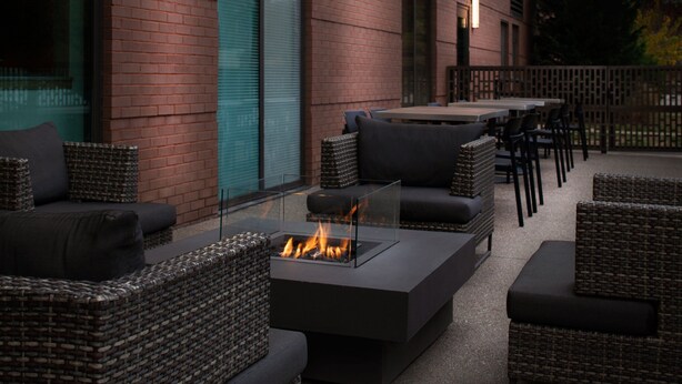 An outdoor patio with wicker furniture, a glass-top table with a fire feature, and a brick building in the background. - Fairfield Inn & Suites by Marriott Charleston (South Charleston)