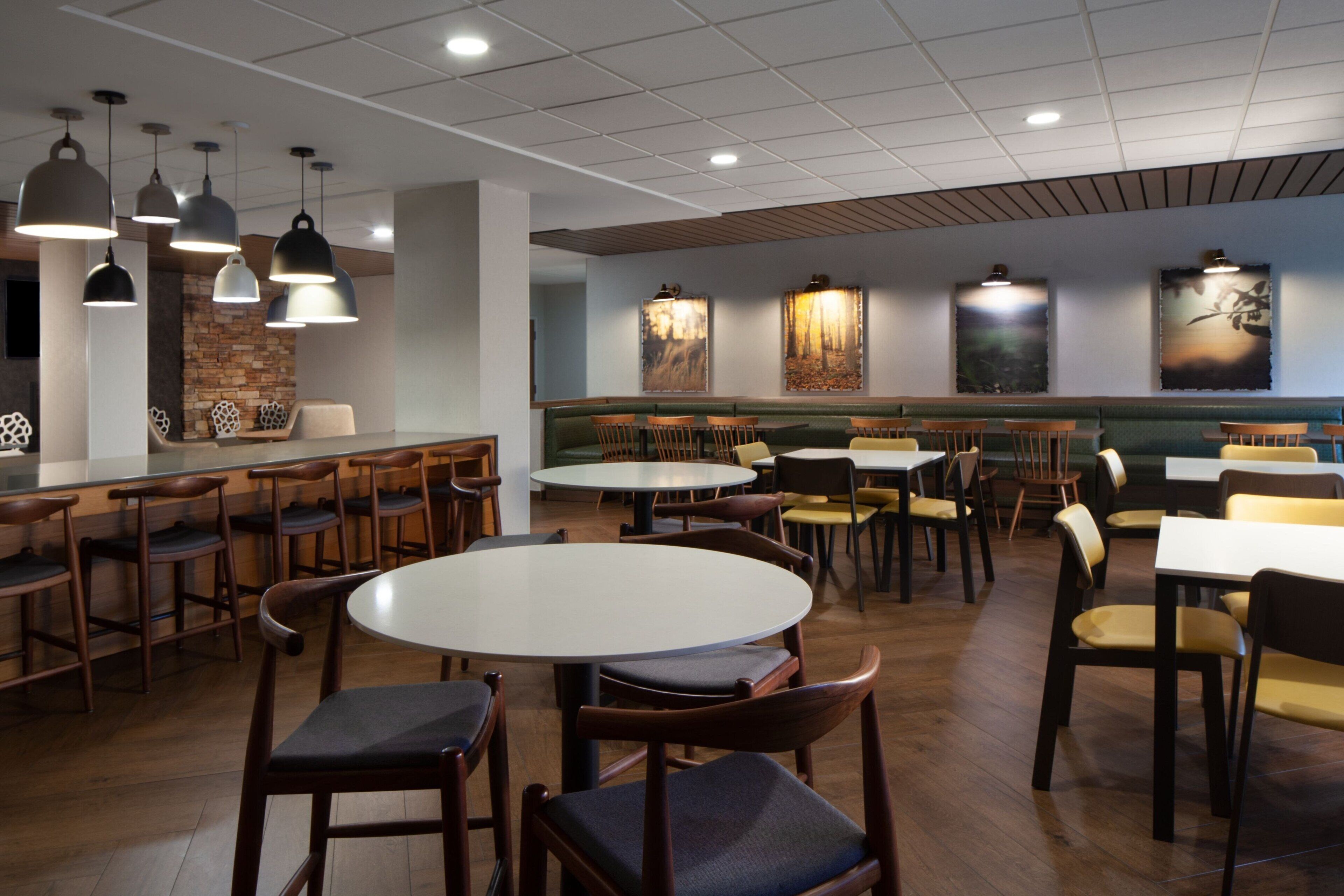 A restaurant with round tables and booths, wooden chairs, pendant lighting, and artwork on the walls.