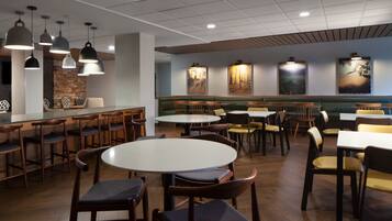 A restaurant with round tables and booths, wooden chairs, pendant lighting, and artwork on the walls.