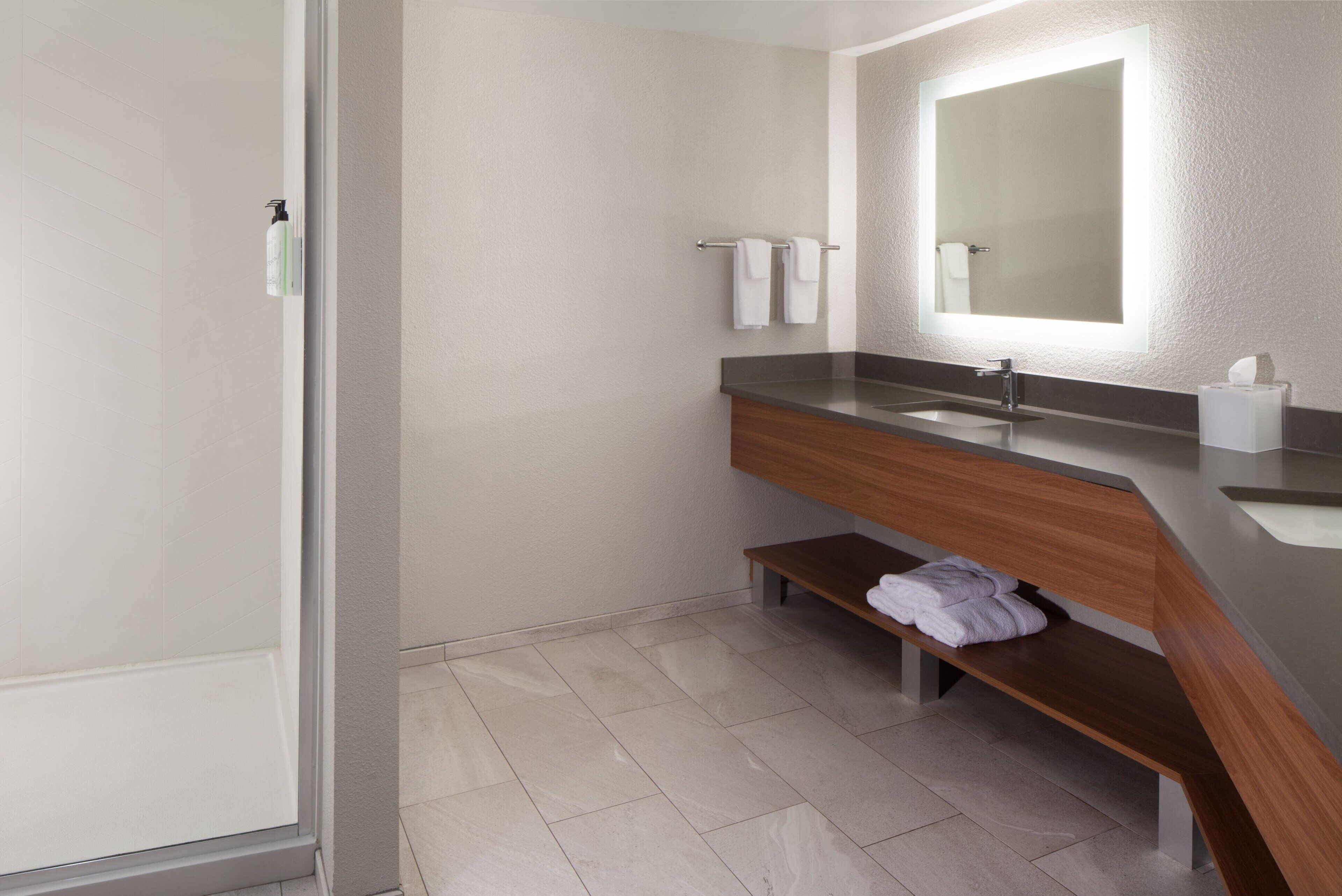 A modern bathroom with a wooden vanity, a large mirror, and a bench.
